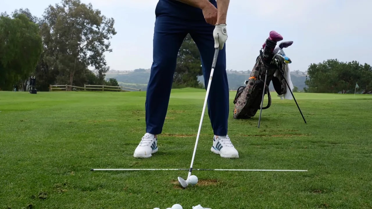 Golfer standing at address with an iron aligned for a compression drill emphasizing early clubface organization