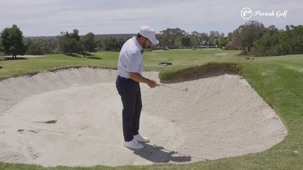 Golfer indicating the fairway bunker lie while choosing the right club to clear the lip