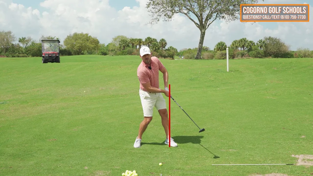 Golf coach demonstrating fairway wood half-swing extension with arms and club reaching outward through impact