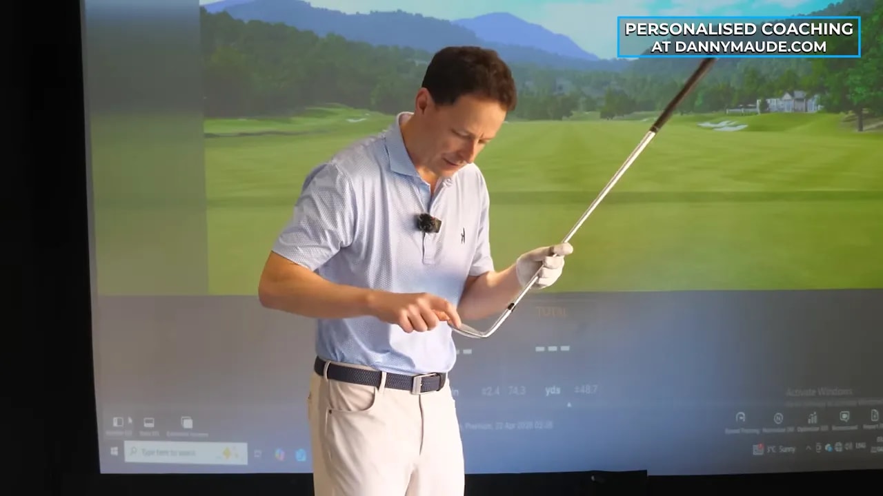 Golf coach holding a club up to the camera while teaching face awareness and strike feedback