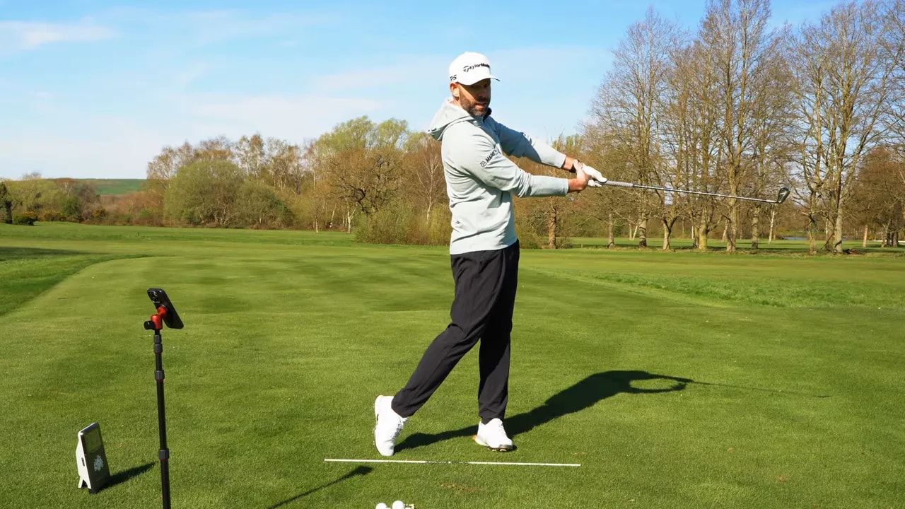 Golfer in a follow-through finish position practicing the 9-to-3 drill on a golf range