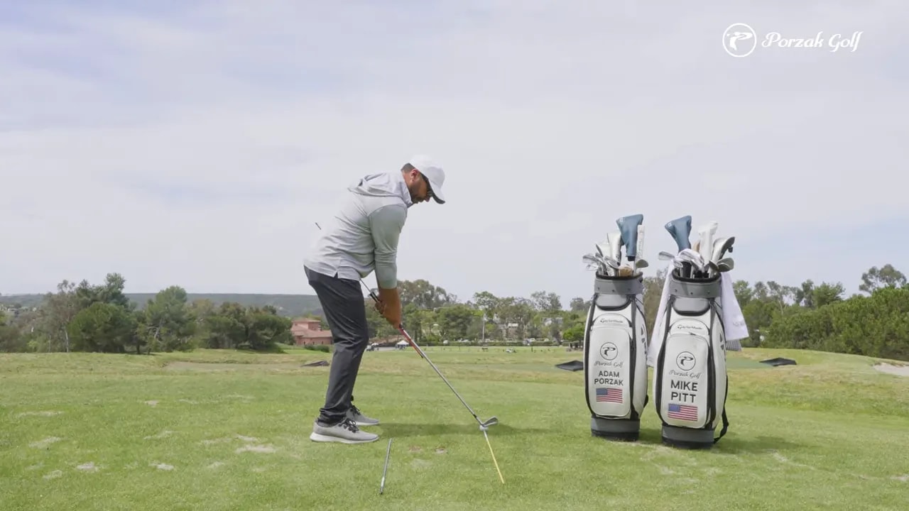 Golfer showing early backswing hand path with alignment rods on the fairway