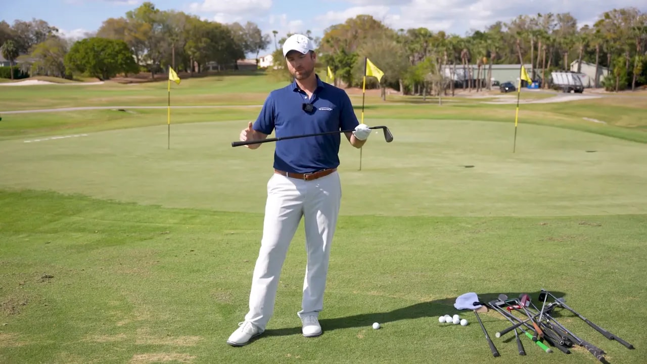 Golf instructor holding a chipper and presenting the stroke model on a practice green