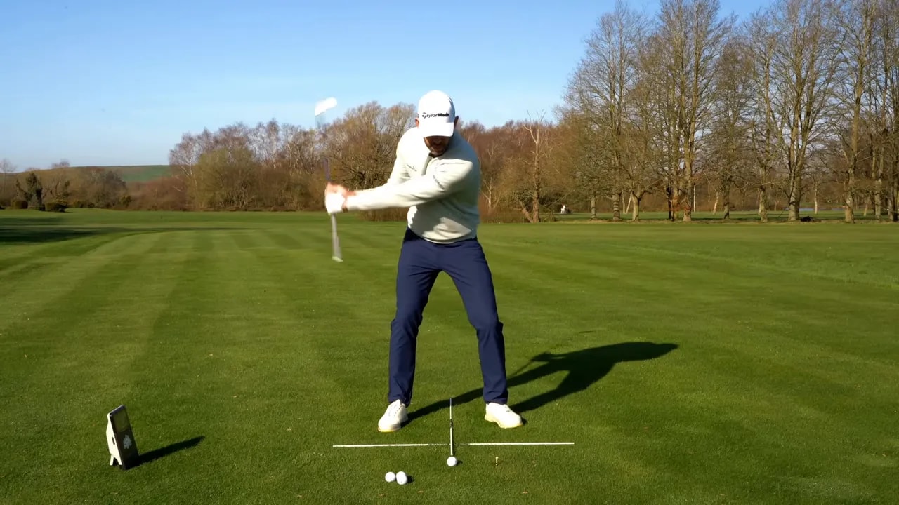 Golfer swinging an iron drill while maintaining the forward low-point focus on grass