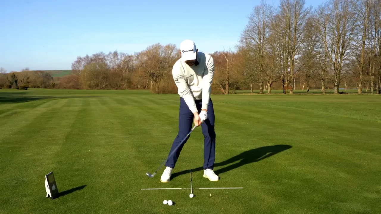 Golfer swinging an iron through a marked low point training line on the range
