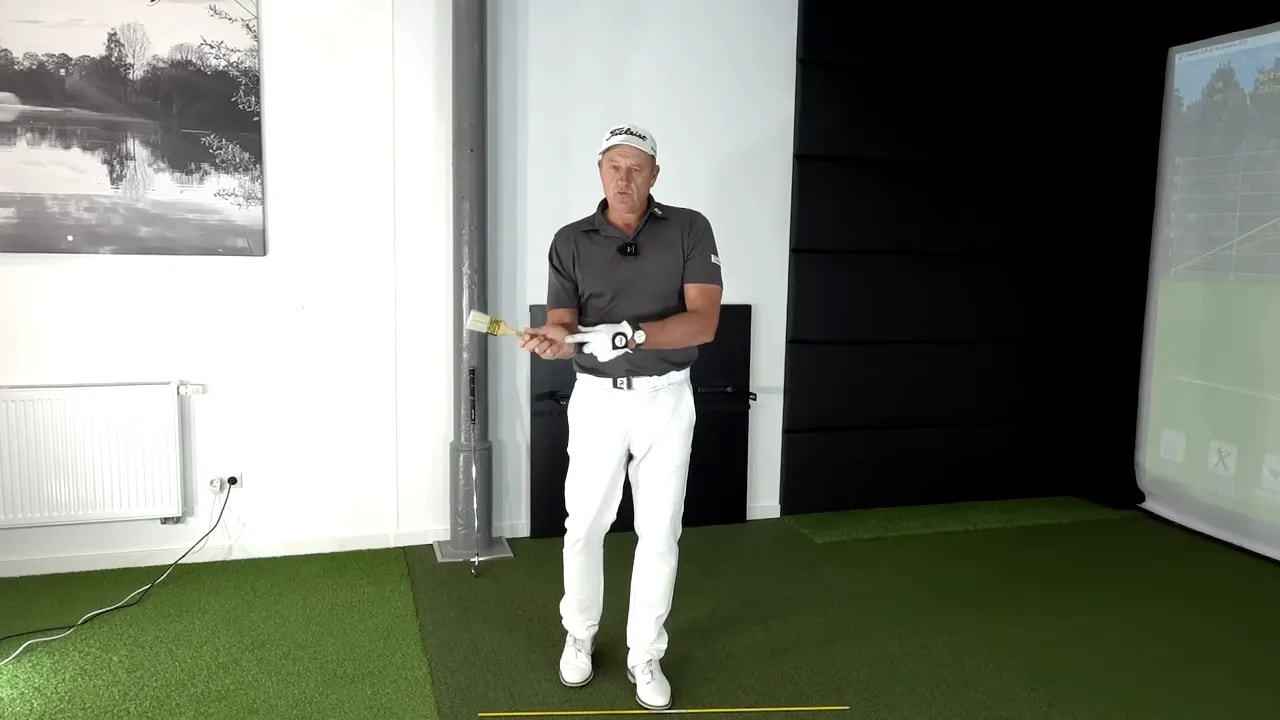 Golf instructor demonstrating the “paint the wall” drill hand position indoors with club aligned to a training line
