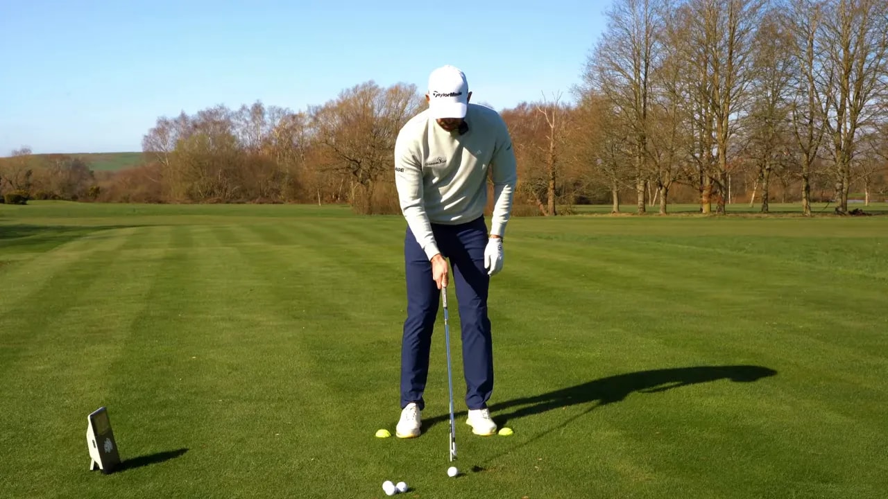 Golfer at address using foot targets and alignment sticks to rehearse a pedal-to-pedal golf drill