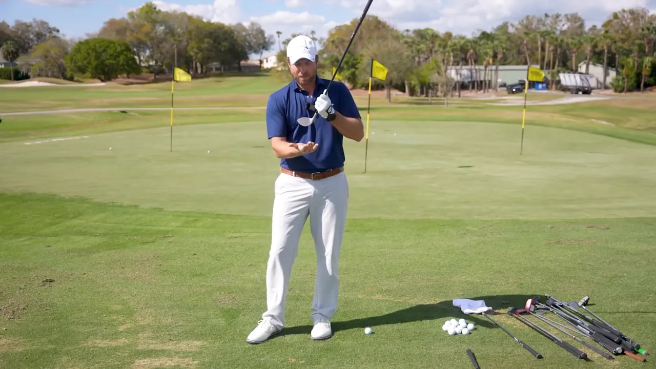 Golfer presenting a chipper while explaining short-game consistency on a golf range
