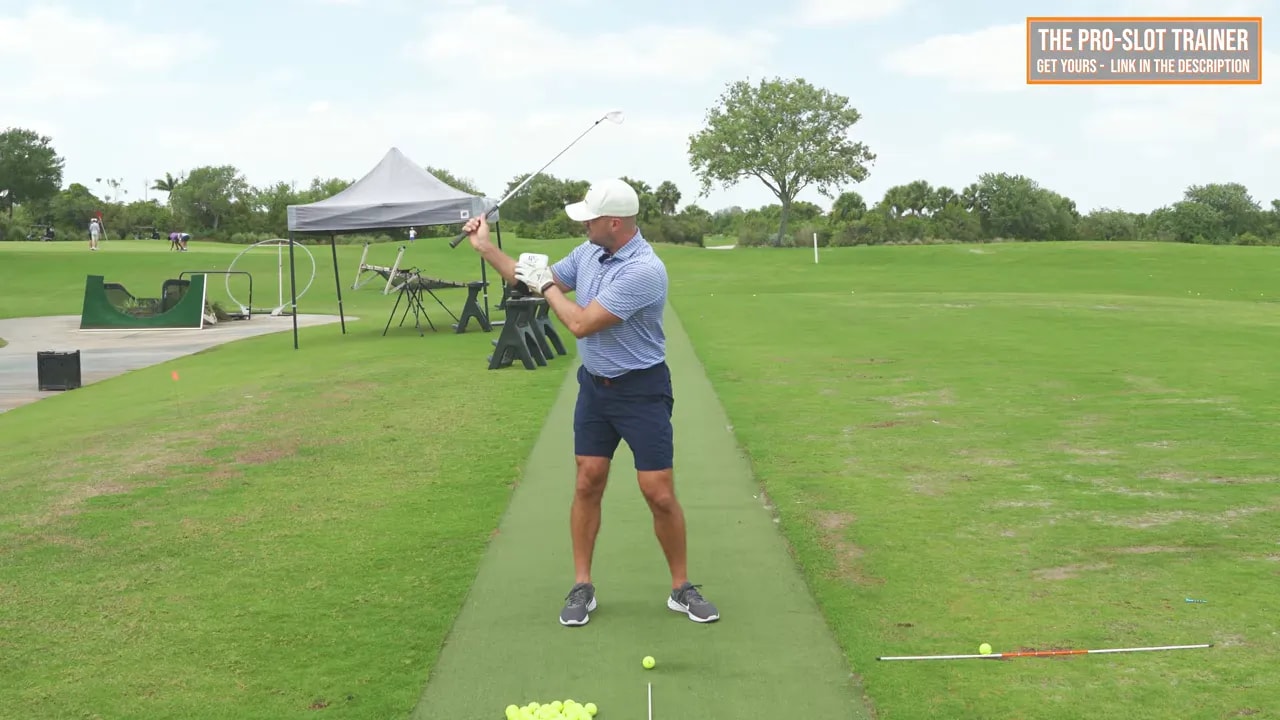 Side view golf coach demonstrating Pro-Slot trainer right-elbow drill for trail-arm width at the range
