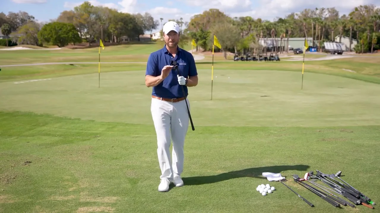 Golf instructor holding a chipper while explaining short-game consistency on a sunny practice range