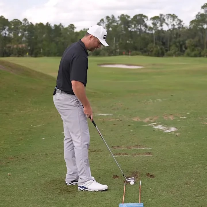 Golfer addressing a ball in a centered neutral station with two alignment markers on the range