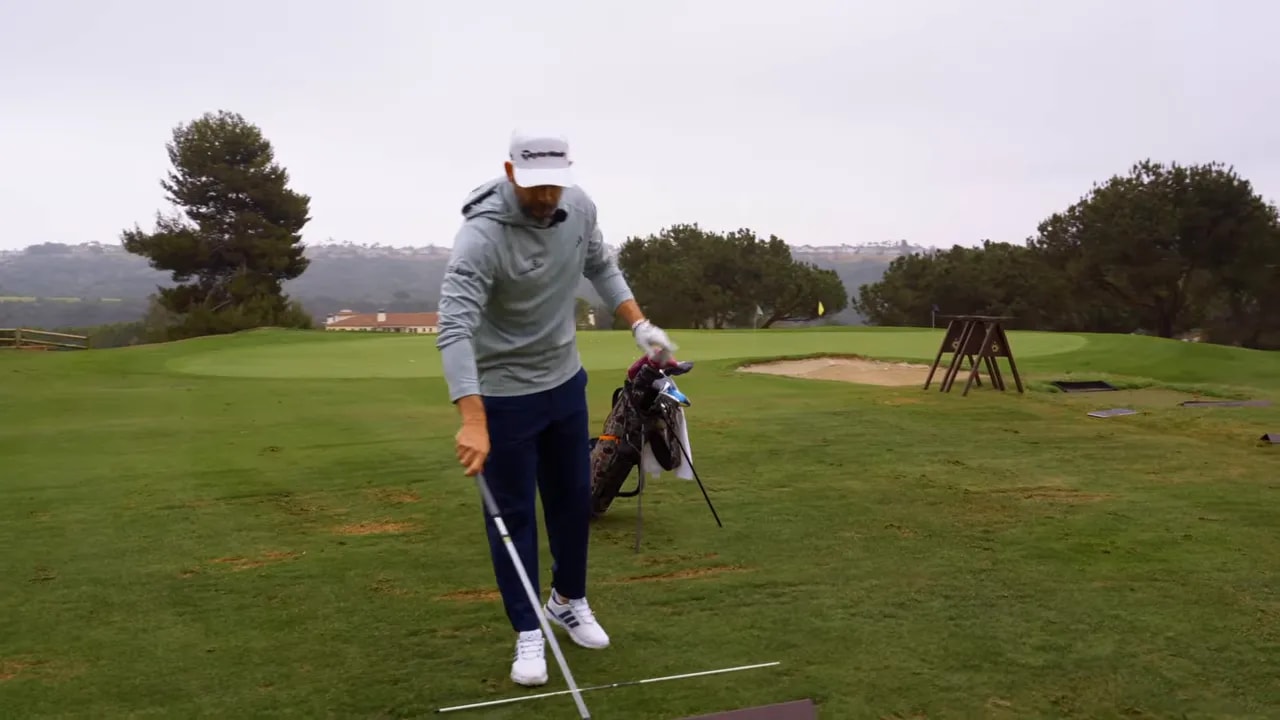 Golfer addressing a ball with an iron while demonstrating a compression drill with training bars