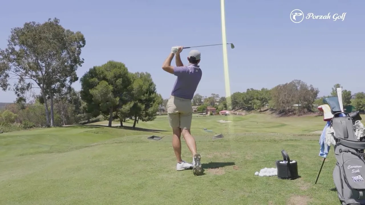 Golfer delivering a controlled iron shot on the range with a flag in the background