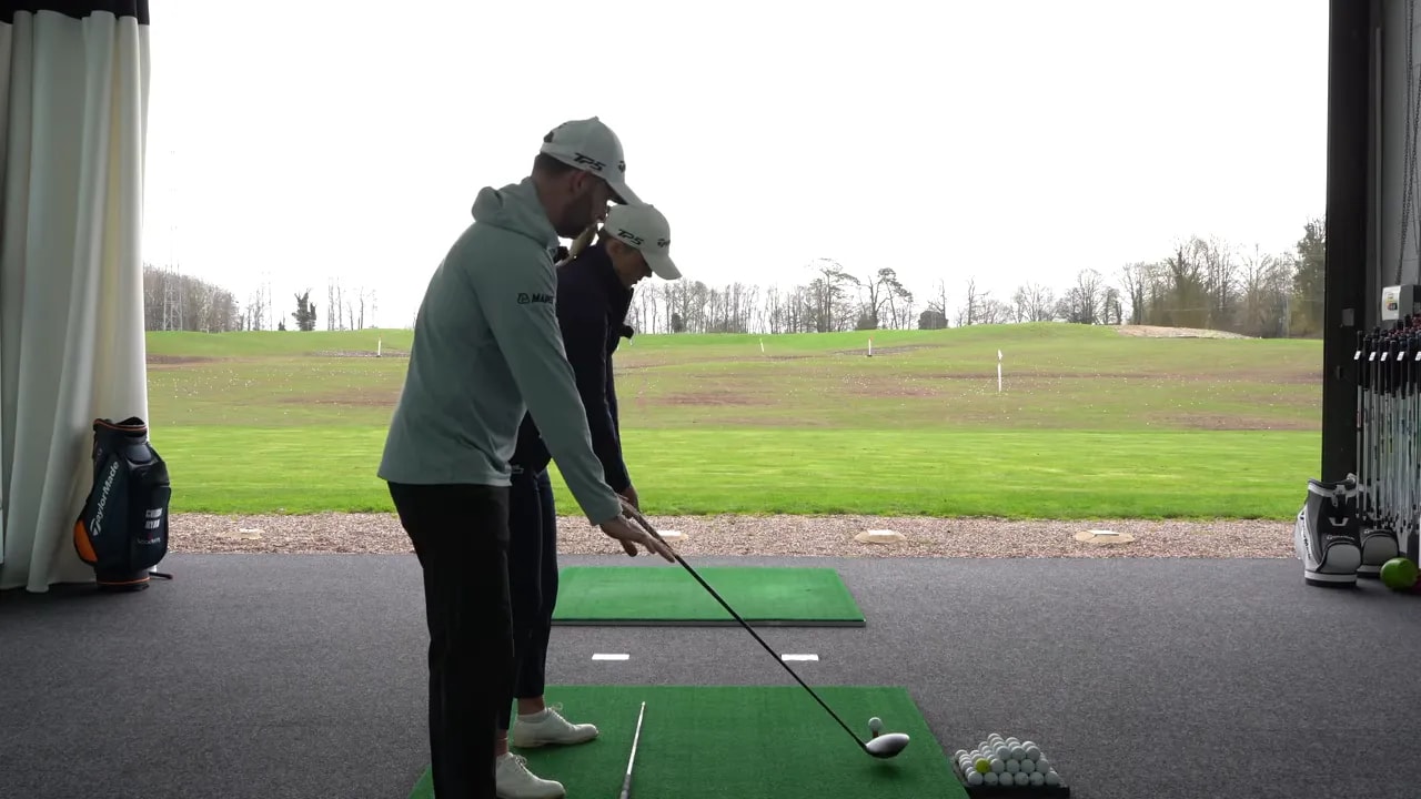 Golfer finishing a driver takeaway drill swing toward the ball on an indoor simulator