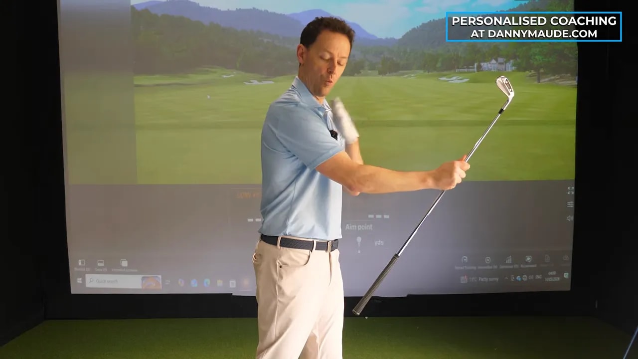 Instructor holding a golf club while demonstrating educated hands swing mechanics in indoor practice bay