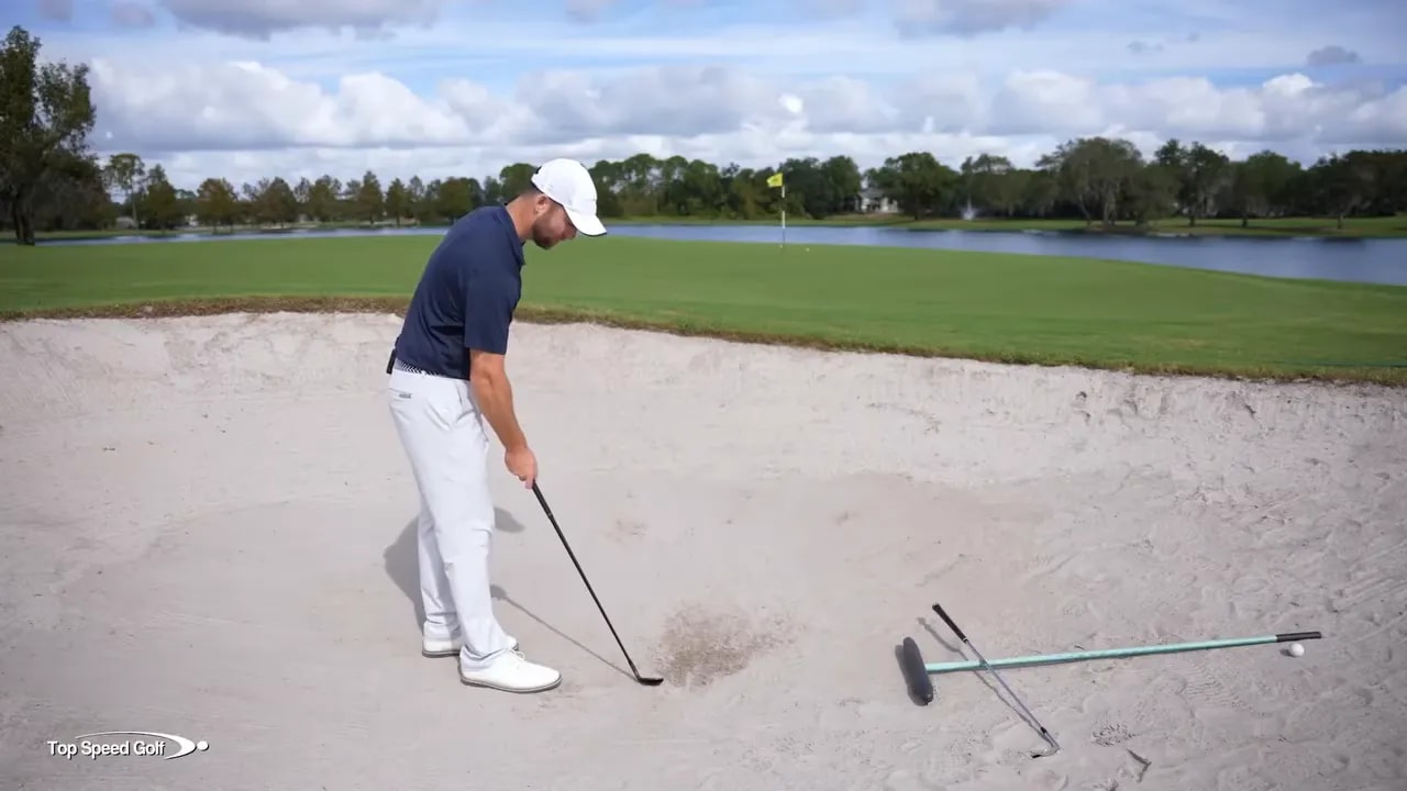 Golf player in a greenside bunker executing a committed sand shot with a wedge