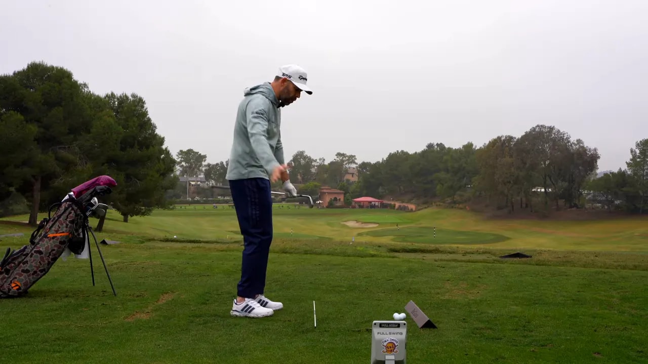 Golfer preparing to hit an iron with a drill setup on the grass at a driving range
