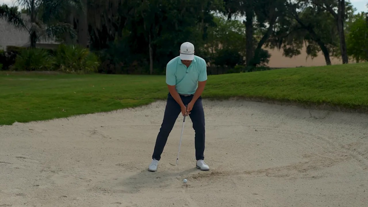Golfer in greenside bunker holding a club in an address position to encourage forward pressure for consistent bunker shots