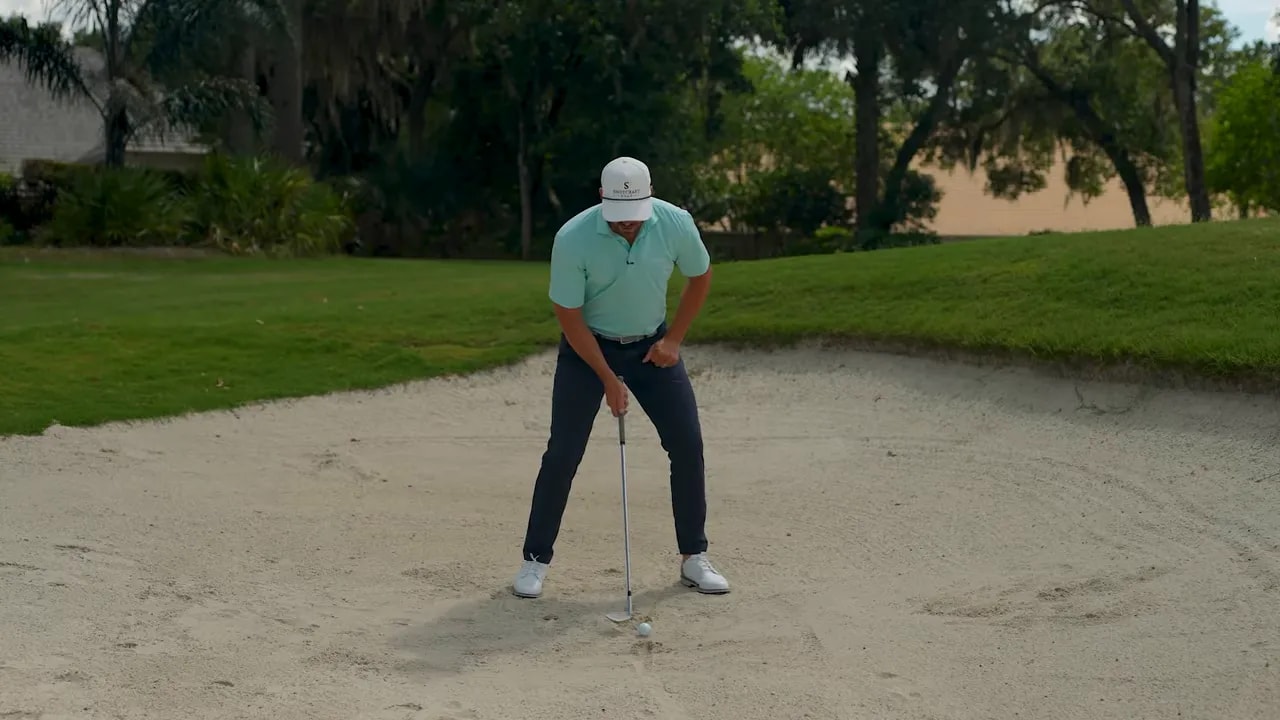 Golfer stance in greenside bunker showing ball position and setup for avoiding playing the ball too far back