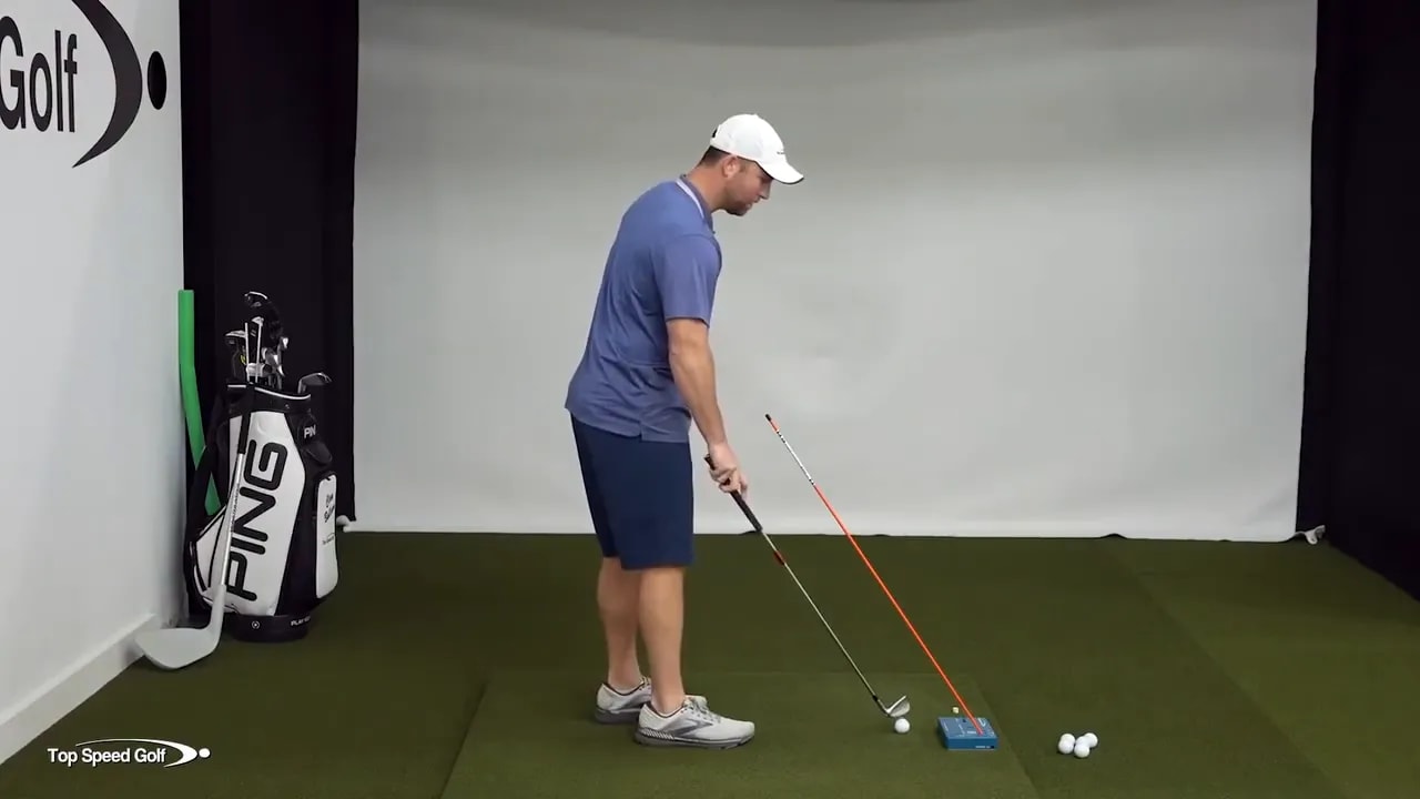 Golfer demonstrating posture retention with an alignment stick training drill in an indoor golf setup