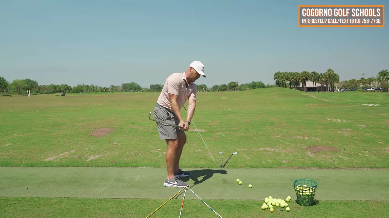 Golfer practicing the through-ball drill from a mini-swing position with training lines and ball basket on the range