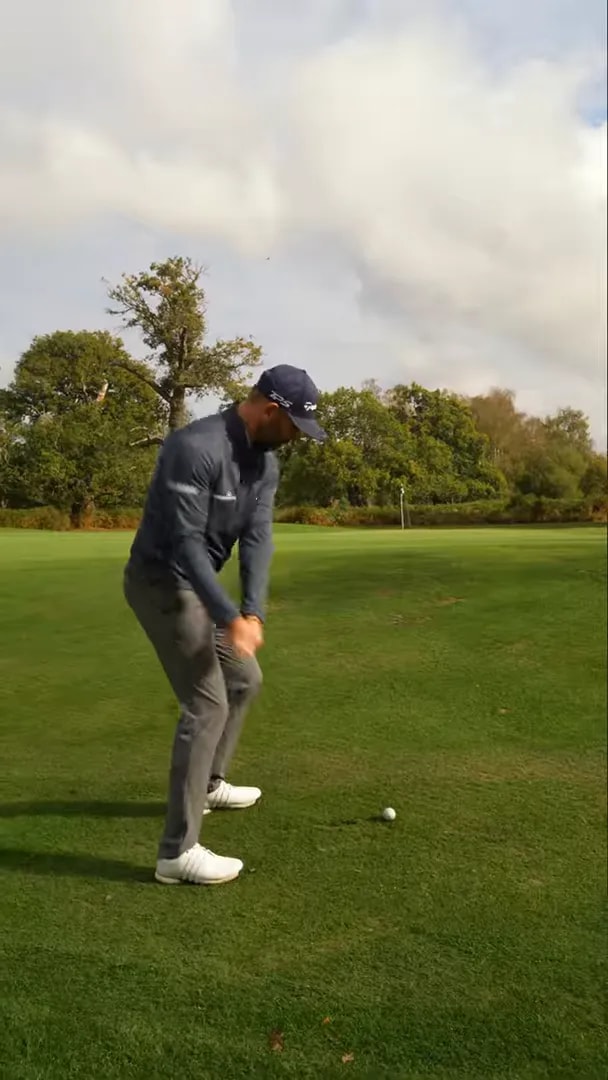 Golfer checking ball position on an upslope green before choosing a high or low chip trajectory
