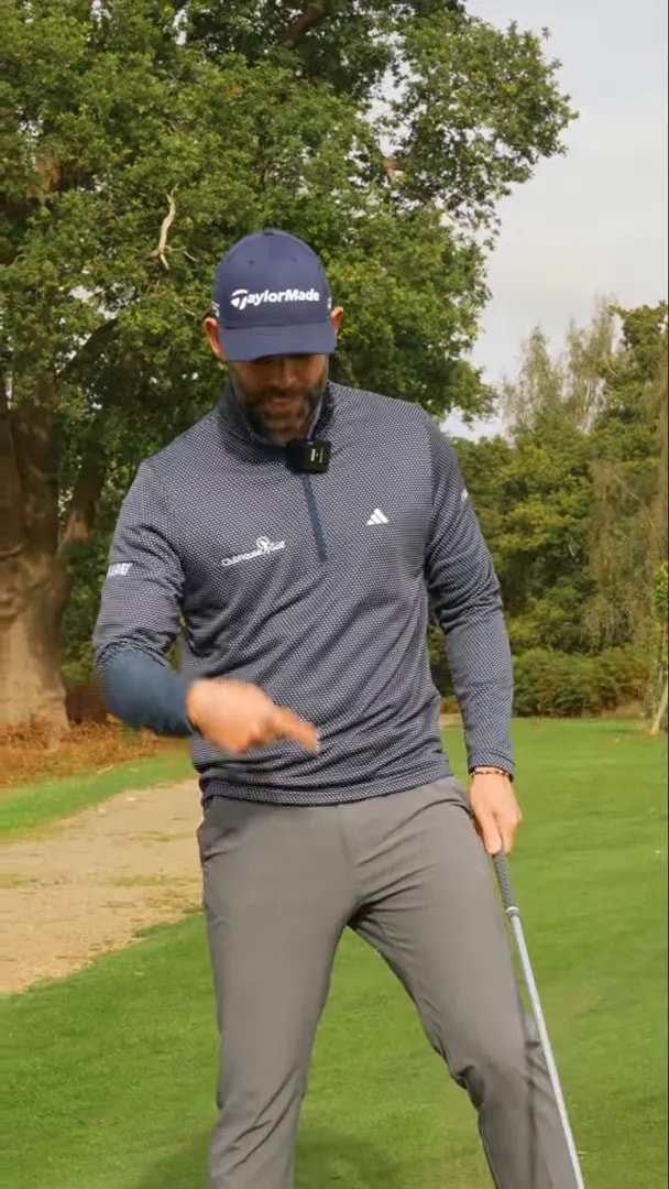 Golfer holding a wedge and pointing to ball position on an upslope green for a high, soft chip