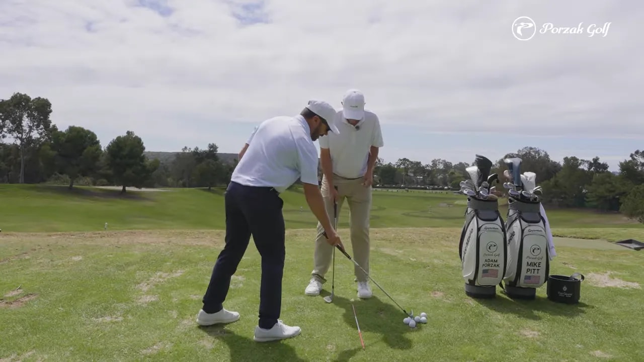 Golf instructor and golfer address a wedge setup on a practice range to demonstrate turning around the center instead of sliding