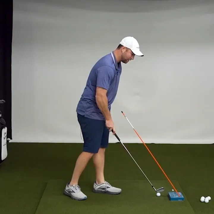 Golfer at address beside an angled alignment stick attached to a blue training block with golf balls nearby