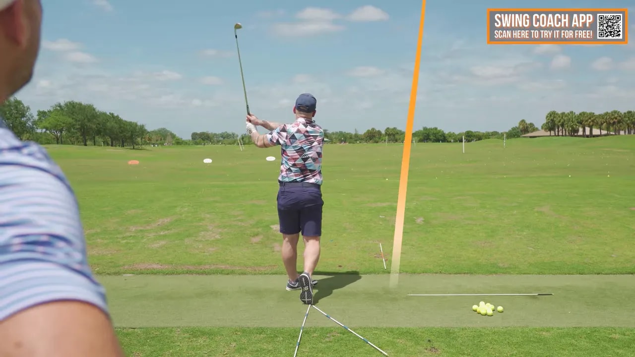 Golfer holding balanced finish on the range with an orange shot tracer showing ball flight