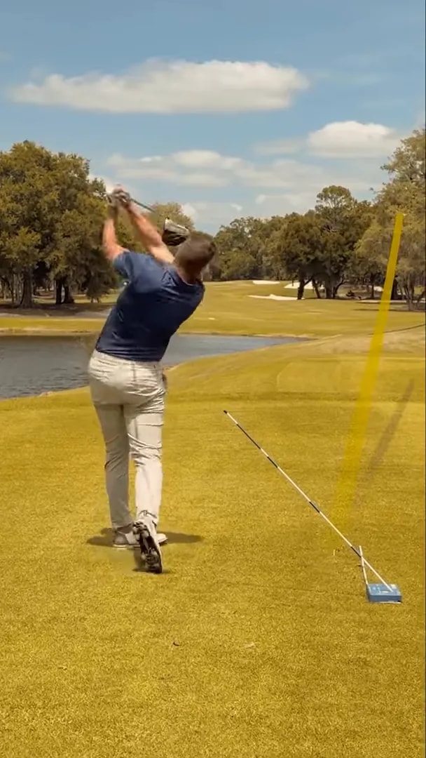 Down-the-line finish position with a yellow ball flight trace and alignment stick on the ground