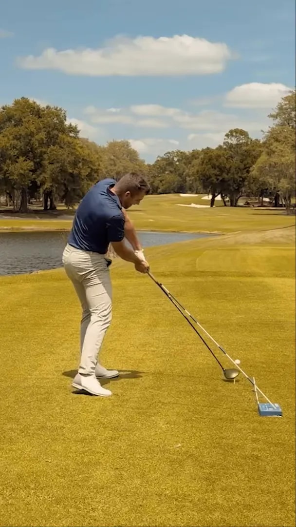 Driver moving through impact beside a ground alignment stick and blue training block showing the intended delivery path