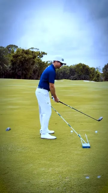 golfer at address with driver next to an angled training aid and alignment stick on the fairway