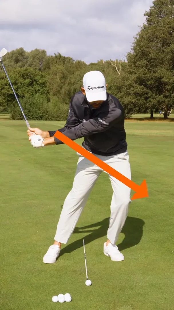 Golfer in downswing with an orange arrow pointing diagonally forward and down toward the lead side