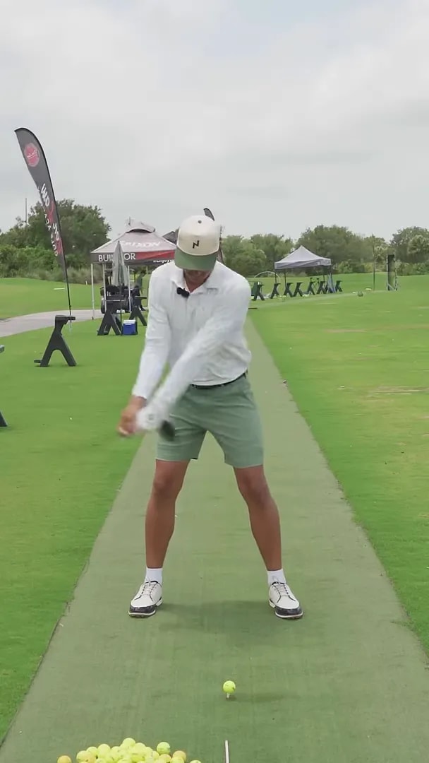 Golfer near the top of the backswing with driver from front view on a practice mat