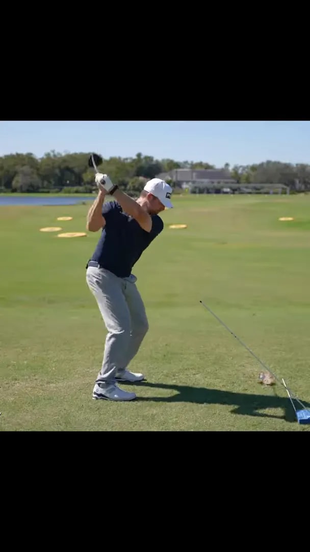 golfer rotating into a full driver follow-through on a practice range