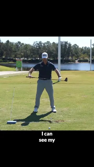 golfer holding club across body near alignment aid on driving range
