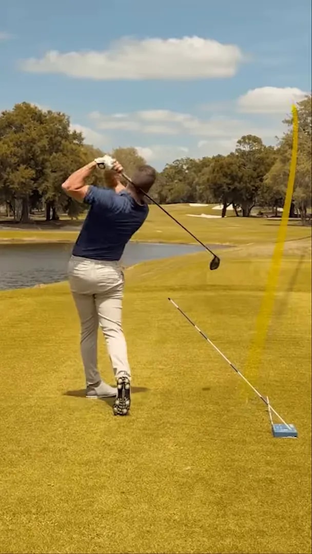 Golfer at address with blue training block and alignment stick set on the ground as a shaft angle reference