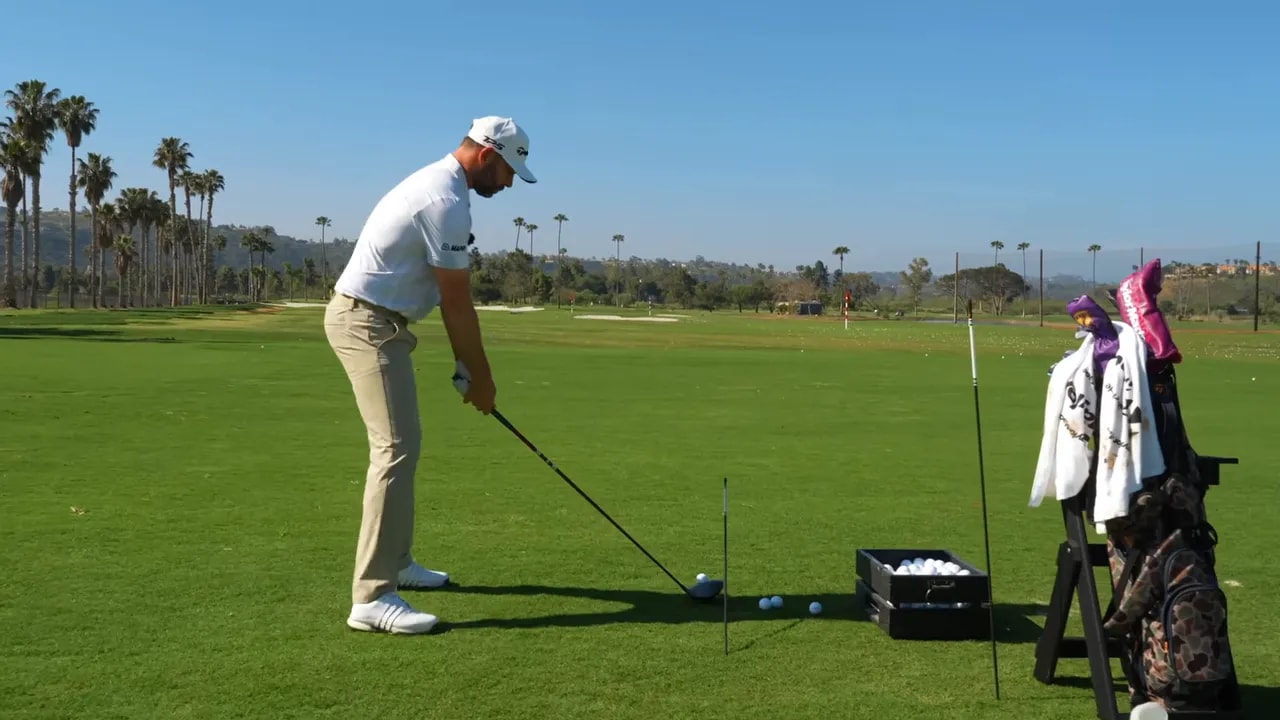 Golfer at address with an alignment stick angled in the ground behind the ball