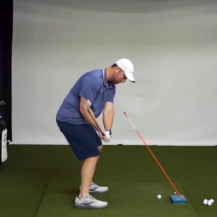 Golfer in downswing with hands close to the body and alignment stick angled beside the ball