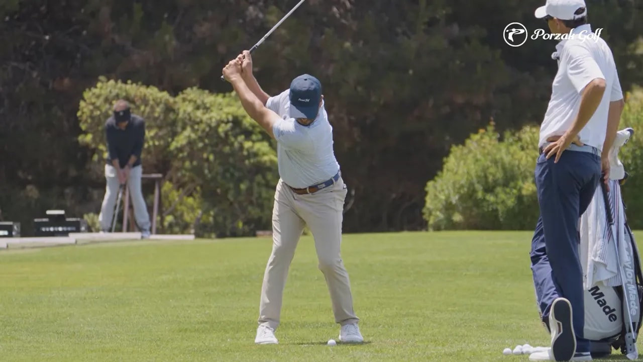 golfer paused near the top of the backswing while another golfer stands nearby