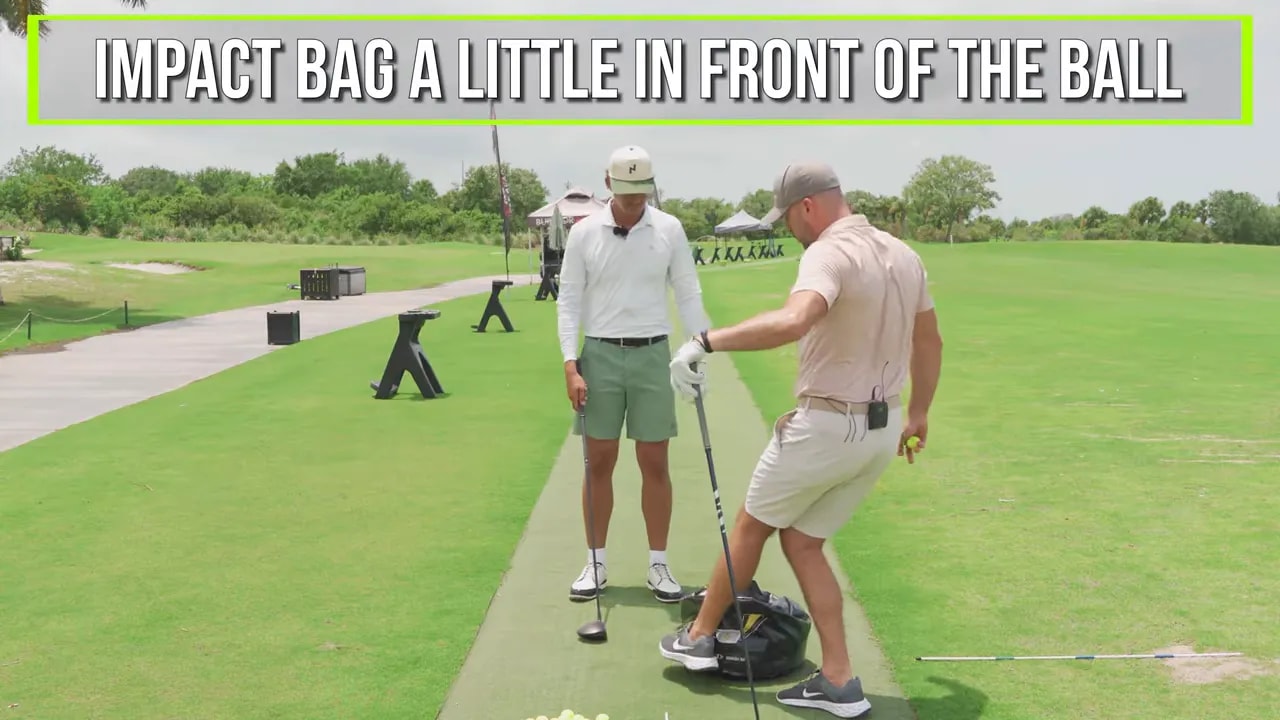 Two golfers standing by an impact bag with on screen text that says impact bag a little in front of the ball