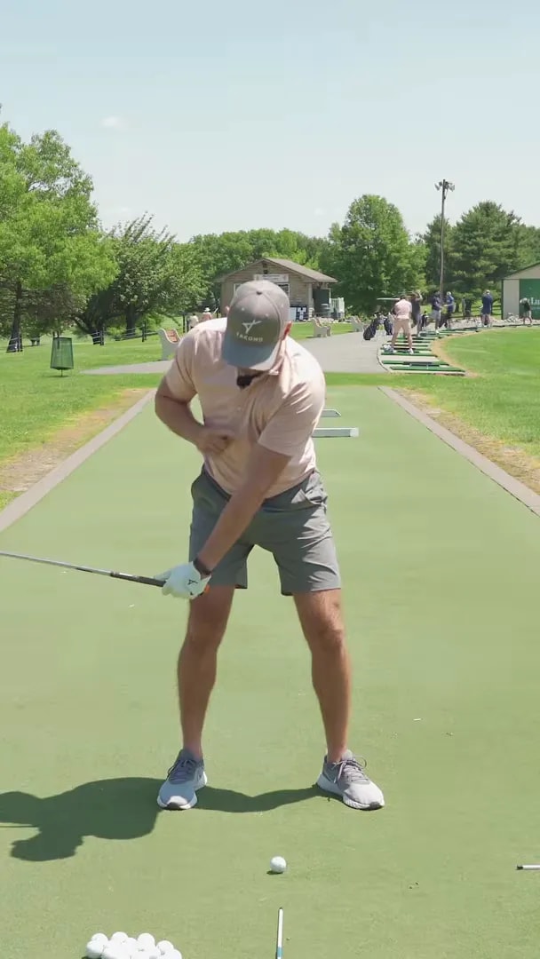Face-on golf swing frame with an orange line highlighting the lead arm angle while the hands stay low