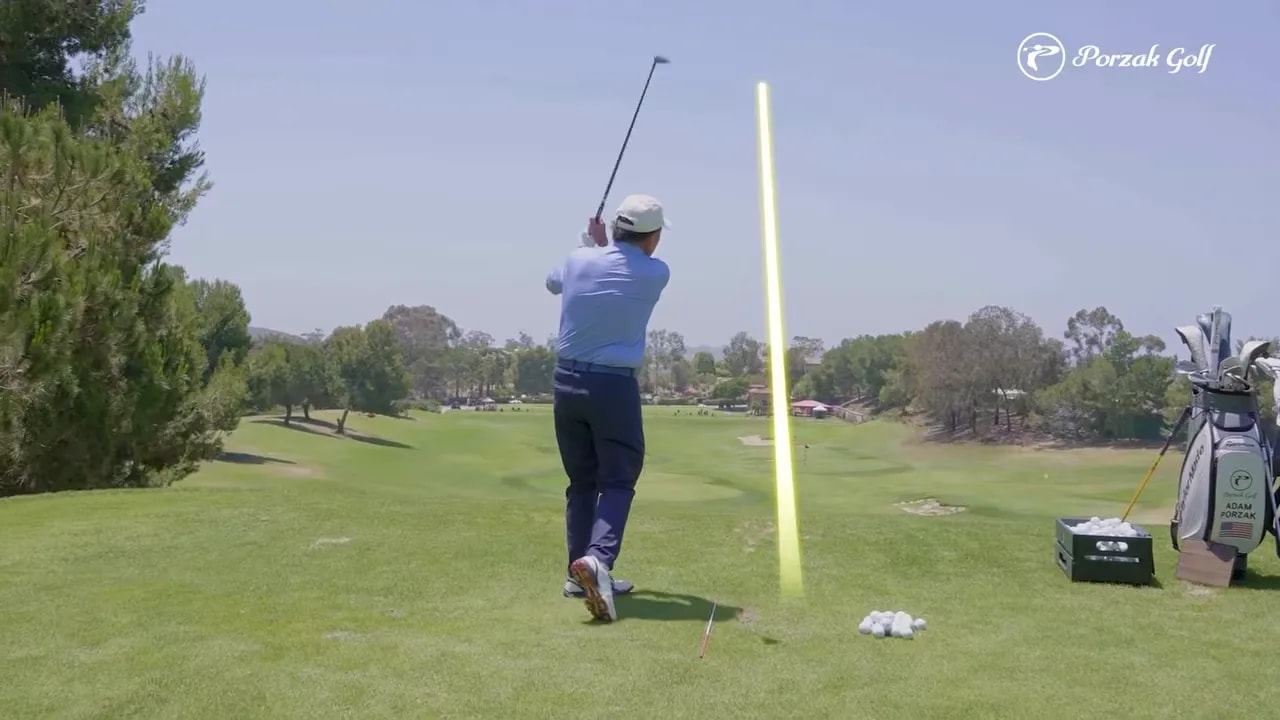 golfer finishing a full swing with a yellow shot tracer rising into the fairway