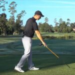golfer pointing a yellow alignment stick toward the ground in front of the ball area