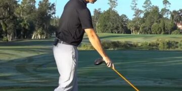 golfer pointing a yellow alignment stick toward the ground in front of the ball area