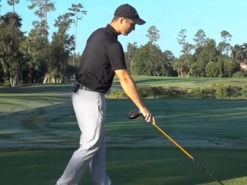 golfer pointing a yellow alignment stick toward the ground in front of the ball area