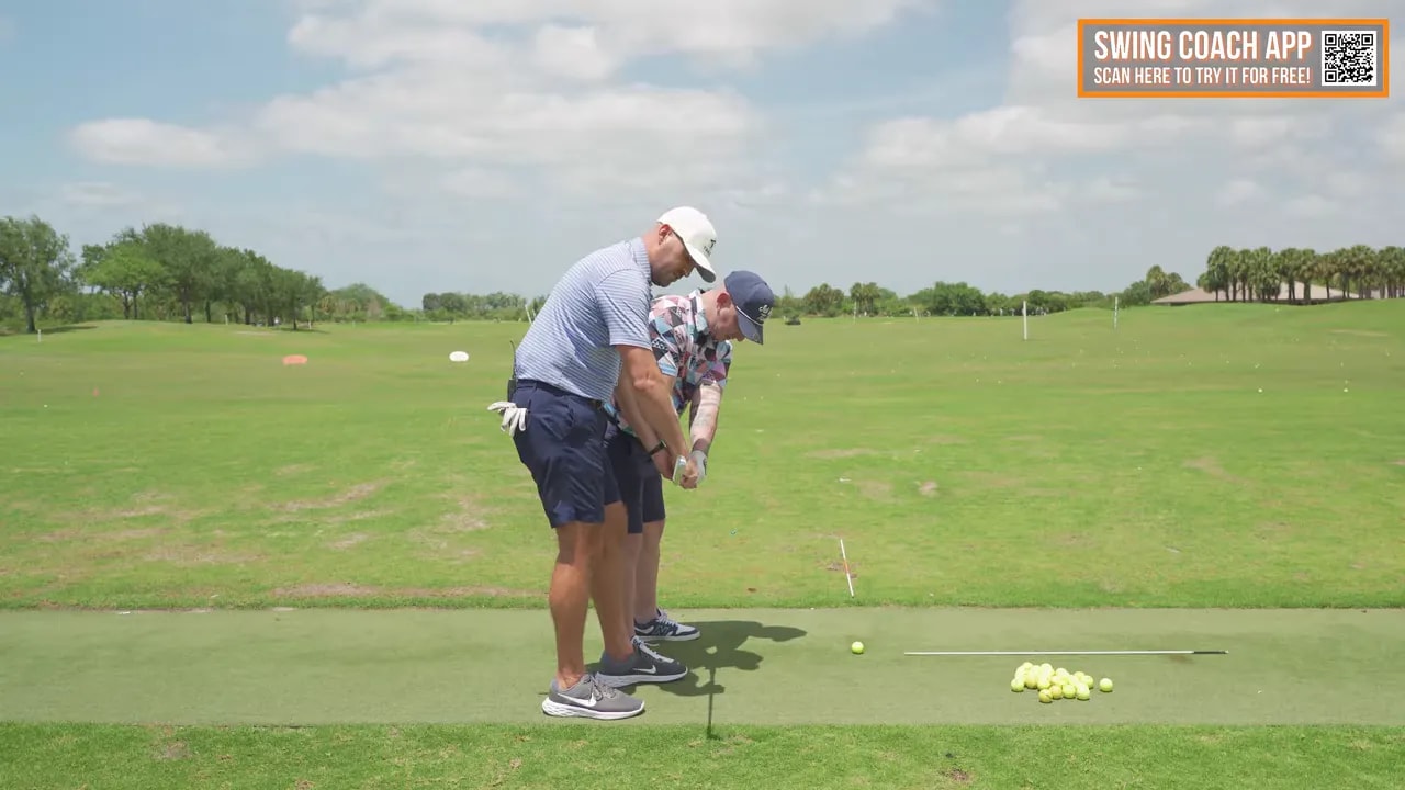 Coach standing behind golfer guiding club and arm position during takeaway drill