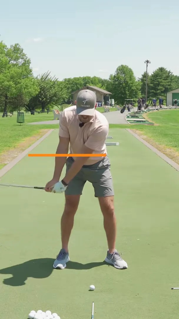Face-on golf swing frame with an orange horizontal line marking a low hand position during the takeaway