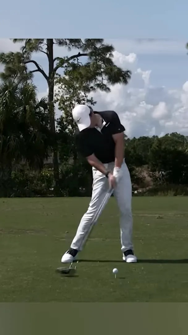 Golfer in black shirt and white pants moving through impact with driver from side view